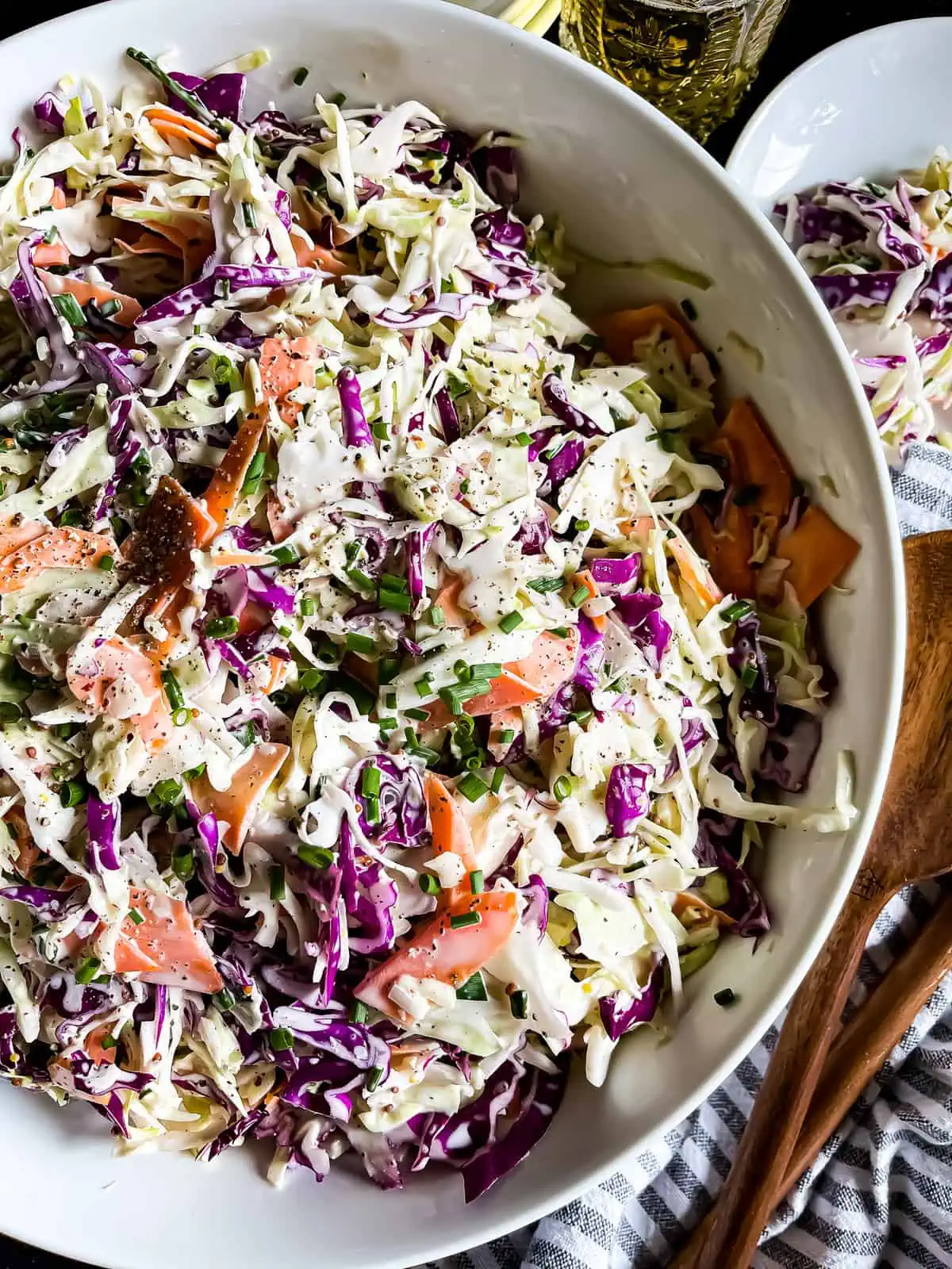 creamy coleslaw in a white serving bowl with serving utensils