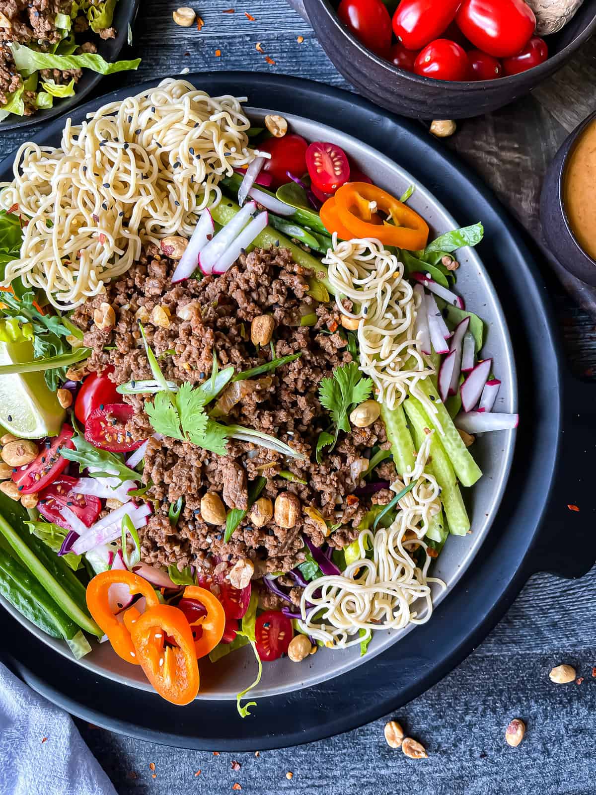 Thai beef salad with peanut dressing. Garnished with fresh veggies, rice noodles, sesame seeds, and extra peanuts