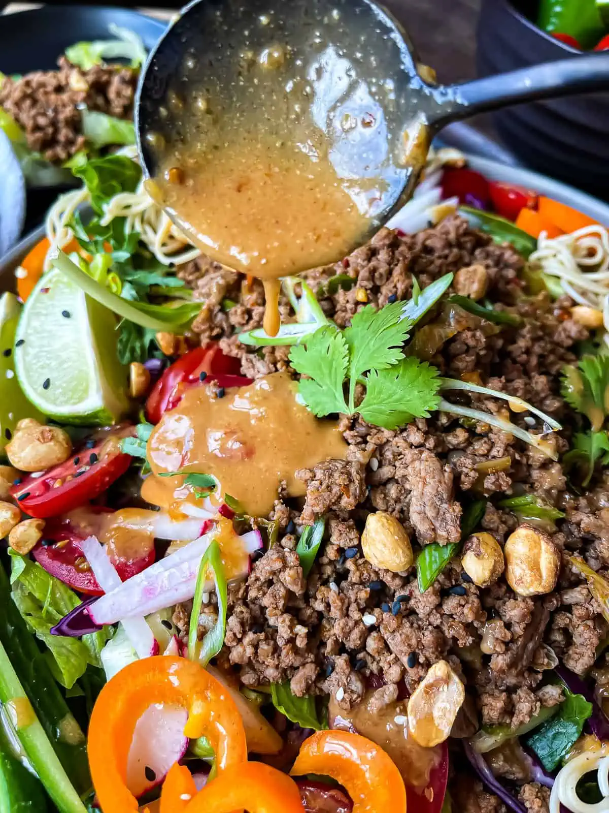 Thai beef salad with peanut dressing. Garnished with fresh veggies, rice noodles, sesame seeds, and extra peanuts