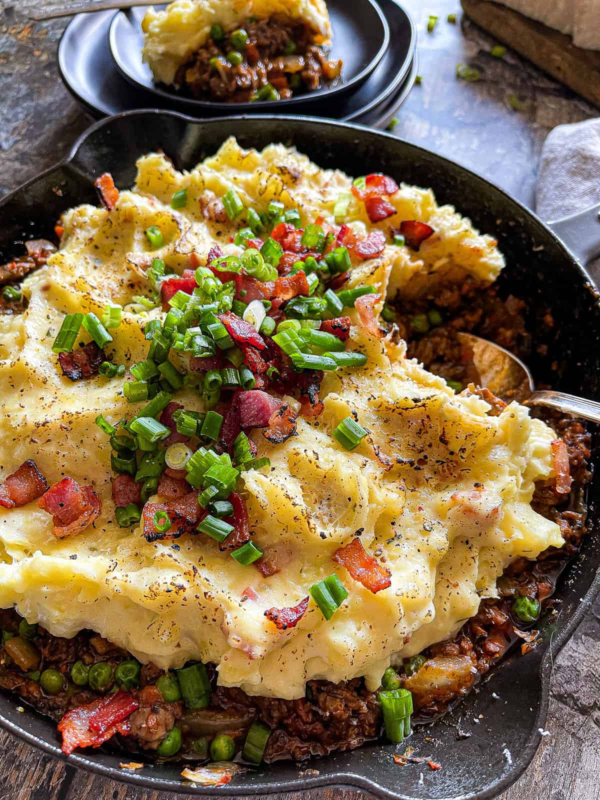 beef shepherd's pie in a large skillet with green onion and bacon garnish