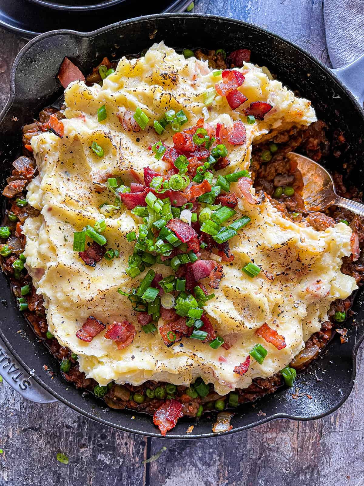 beef shepherd's pie in a large skillet with green onion and bacon garnish