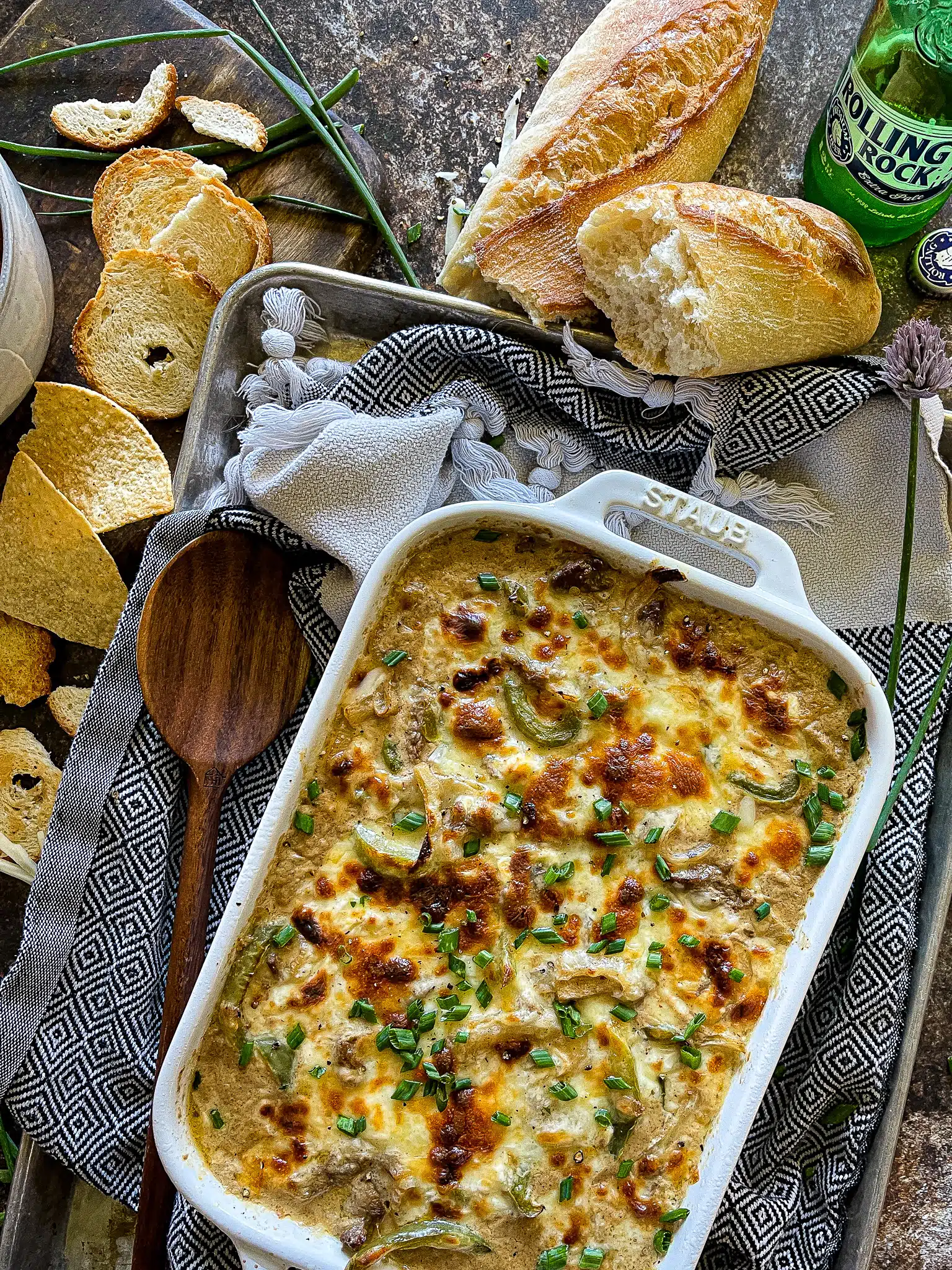 philly cheesesteak dip in a baking dish and garnished with chips and crusty bread for dipping